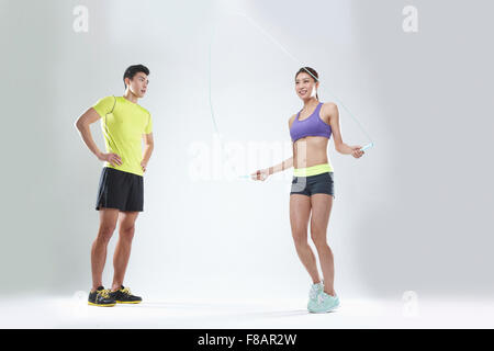 Man in sportswear standing with hands on waists, woman in sportswear jumping rope with a smile Stock Photo