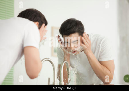 Portrait of young man washing his face at sink in bathroom Stock Photo