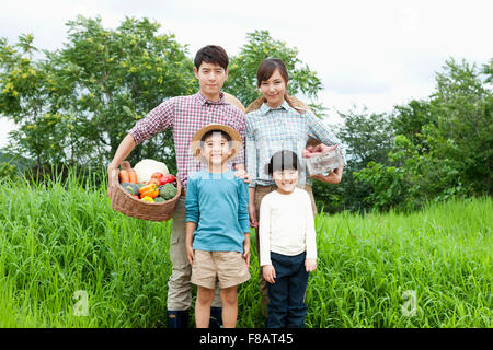 Happy family standing with fresh vegetables staring at front in country Stock Photo