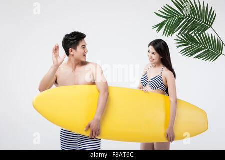 Couple in swimsuits holding a surfing board with palm leaves Stock Photo