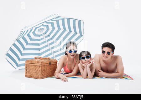 Portrait of family wearing sunglasses and swimsuits under a parasol Stock Photo