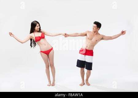 Couple in swimsuits standing hand in hand opening arms face to face Stock Photo