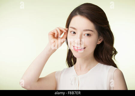 Korean woman with long wavy hair in white sleeveless shirt drawing her hair back over her ear and looking aside with a smile Stock Photo