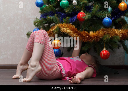 little girl lying on her back under the Christmas tree Stock Photo