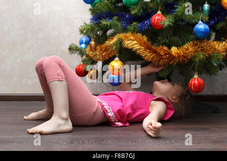 little girl lying on her back under the Christmas tree Stock Photo