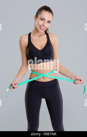 Beautiful positive fitness girl in sportwear taking body measurements over grey background Stock Photo