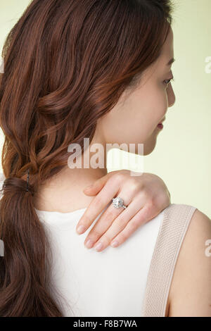Back appearance of Korean woman with pony tail hair in white sleeveless shirt putting her hand on her shoulder with a ring on Stock Photo