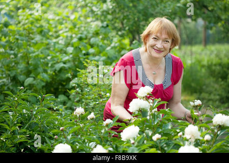 Happy mature woman in yard gardening with peony plant Stock Photo