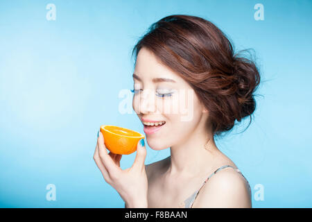 Woman with a smile holding orange in hand close to her mouth with her eyes closed Stock Photo