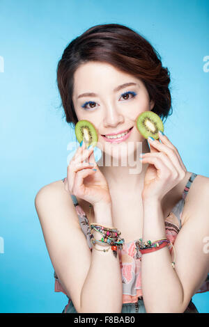 Woman with a smile holding kiwi slices in both hand close to her cheek Stock Photo