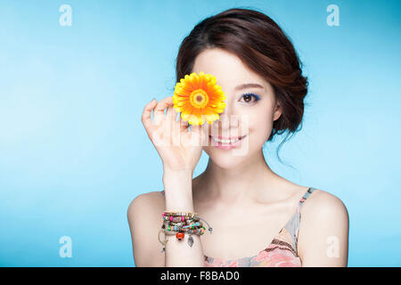 Woman in summer wear covering her eye with a flower and smiling Stock Photo