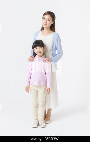 Young Korean mother standing and putting her hands on her daughter's shoulders Stock Photo