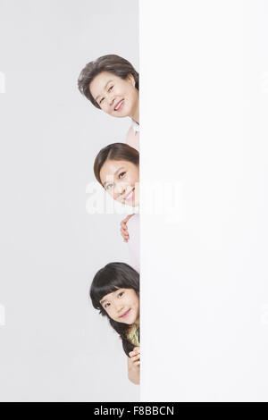 Mother, daughter, and granddaughter hiding behind the white copy space and showing their faces Stock Photo