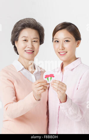 Mother and grown-up daughter holding a picture of carnation together and smiling Stock Photo
