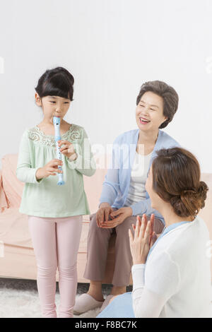Granddaughter playing an instrument and grandmother and mother being happy looking at her Stock Photo