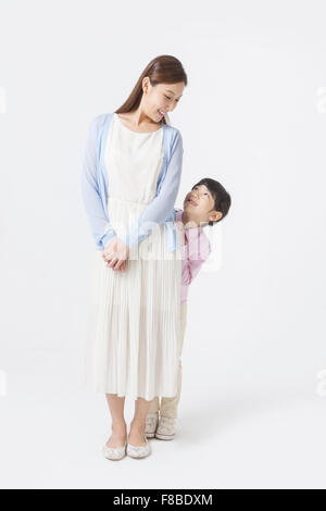 Daughter standing and hiding behind her mother and mother looking at the daughter Stock Photo