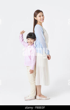 Mother and daughter standing back to back each other and smiling forward and the daughter putting her hand up Stock Photo