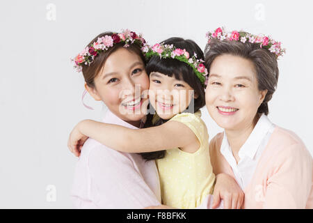 Mother and daughter hugging each other and grandmother right next to them all wearing flower crowns and staring forward with a Stock Photo