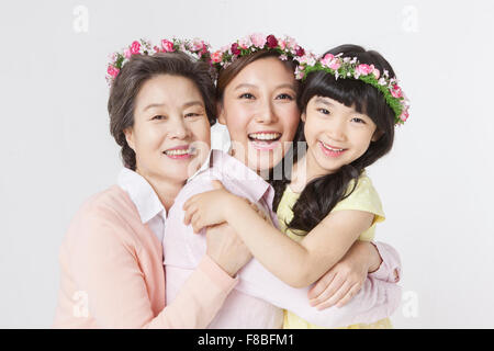Mother, daughter, grandmother hugging each other and smiling forward with flower crowns on their head Stock Photo