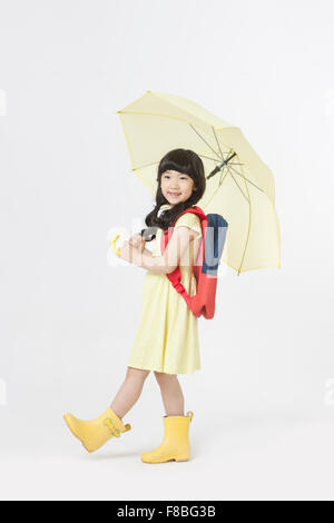 Young girl in yellow dress and rain boots with backpack holding an yellow umbrella and walking Stock Photo