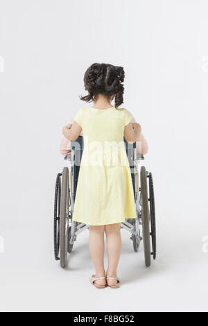 Back appearance of young girl standing behind her grandmother seated on a wheel chair Stock Photo