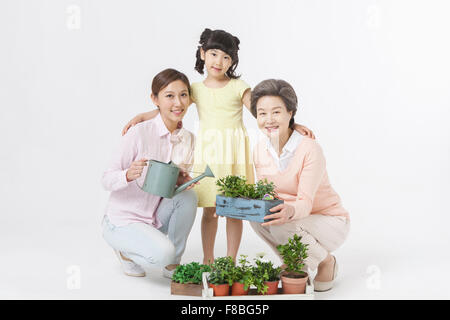 Young girl standing between her mother watering plants and her grandmother holding the plants Stock Photo