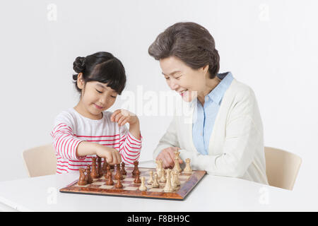 Young girl and her grandmother seated at table playing chess Stock Photo