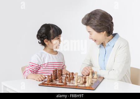 Young girl and her grandmother seated at table playing chess together Stock Photo