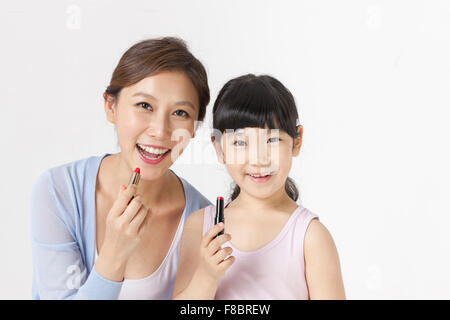 Young girl and her mother holding a lipstick each and staring forward with a smile Stock Photo