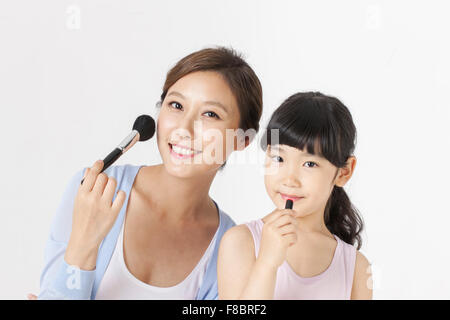 Young girl holding a lipstick and her mother holding a make-up brush both staring forward with a smile Stock Photo