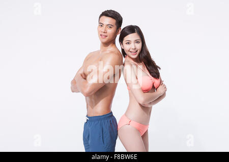 Muscular man in swimming pants and woman with long hair in bikini standing back to back each other with their arms folded Stock Photo