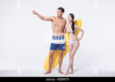 Muscular man and woman in swimming wear standing with a surfing board with man's finger pointing Stock Photo