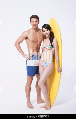 Muscular man and woman in swimming wear standing and staring forward with a surfing board standing and smiling Stock Photo