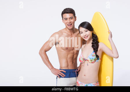 Muscular man and woman in swimming wear close to each other with a surfing board behind the woman Stock Photo