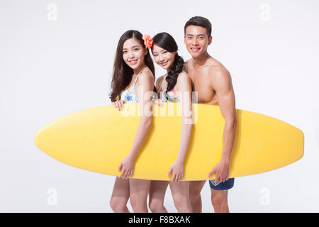 Two women in bikini and a man in swimming pants holding a surfing board together Stock Photo