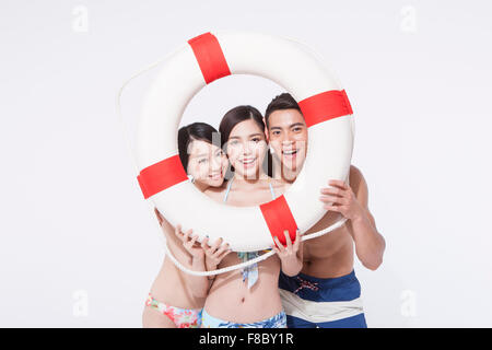 Two women and a man in beach wear holding a lifebelt close to their faces and looking through it Stock Photo