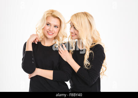 Attractive cheerful young blonde sisters twins talking and looking away over white background Stock Photo