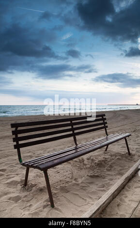 Empty wooden bench stands on sandy beach, Mediterranean sea coast, Spain Stock Photo