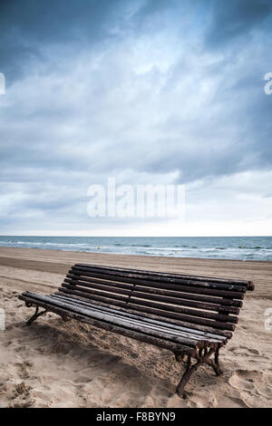 Old empty wooden bench stands on sandy beach, Mediterranean sea coast, Spain Stock Photo