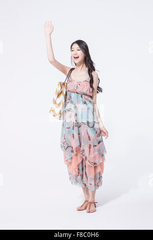 Woman with long hair in long dress and sandals with a bag on her shoulder standing and waving her hand Stock Photo