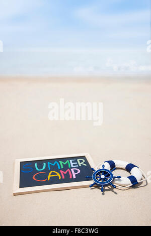 Copy space with word SUMMER CAMP written on miniature blackboard on sand in out-focused effect with the background of beach Stock Photo