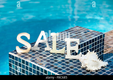 SALE letters with white shell standing on tiles with the background of swimming pool Stock Photo