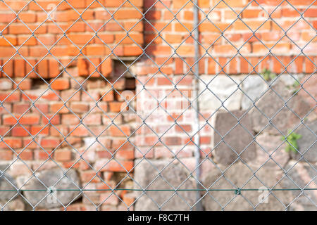 Wire fence in front of brick wall, shallow depth of field. Stock Photo
