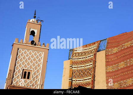 Moroccan Carpets for sale at a shop and minaret of a mosque in Marrakesh Stock Photo