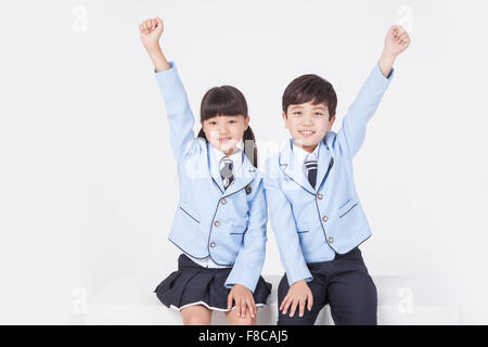 Elementary school age girl and boy sitting together with their hands up and staring forward with a smile Stock Photo