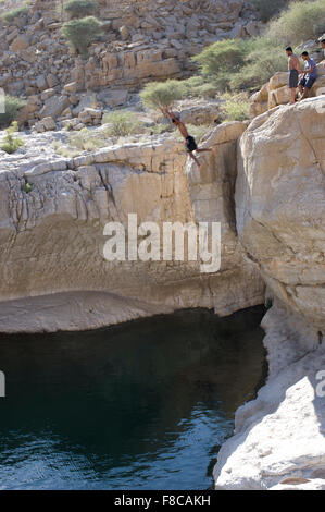 Man jumps from a cliff at Wadi Bani Khalid, a natural canyon formation of rocks and crystal clear pools Stock Photo