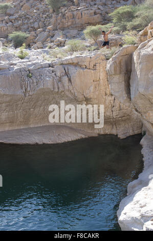 Man jumps from a cliff at Wadi Bani Khalid, a natural canyon formation of rocks and crystal clear pools Stock Photo