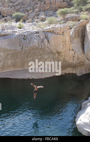 Man jumps from a cliff at Wadi Bani Khalid, a natural canyon formation of rocks and crystal clear pools Stock Photo