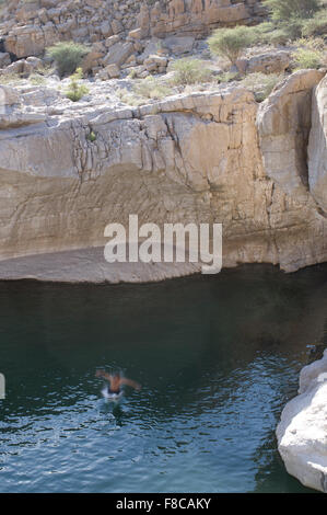 Man jumps from a cliff at Wadi Bani Khalid, a natural canyon formation of rocks and crystal clear pools Stock Photo