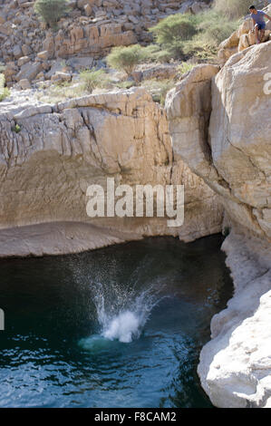 Man jumps from a cliff at Wadi Bani Khalid, a natural canyon formation of rocks and crystal clear pools Stock Photo